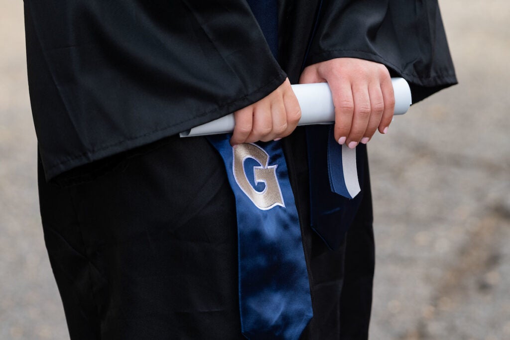 Graduate in commencement gown holding paper diploma with a 