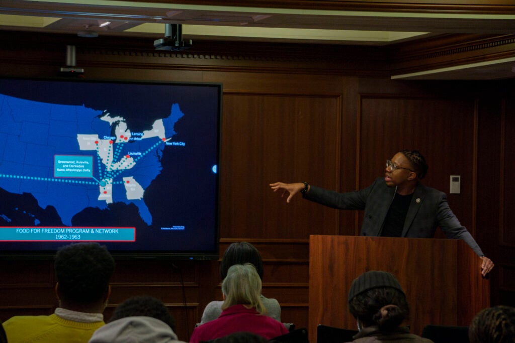 Dr. Bobby J Smith II stands at a podium in front of an audience, pointing at a screen showing a map of the United States overlaid with the Food For Freedom Program & Network