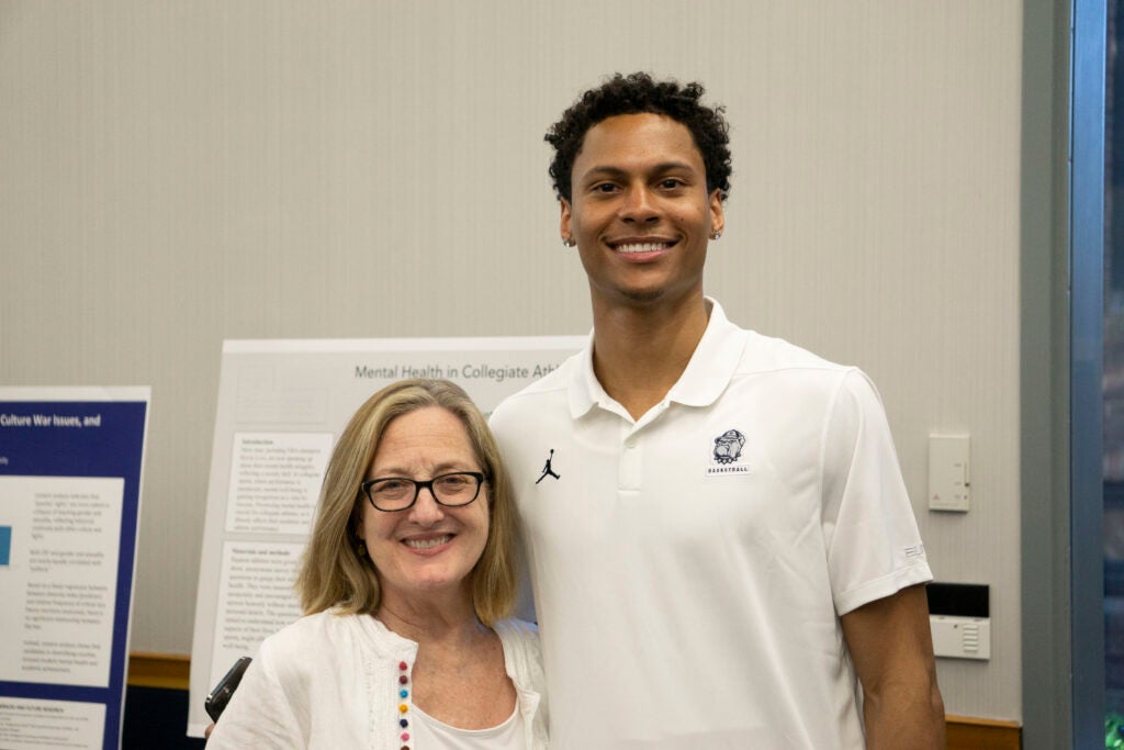 Senior Wayne Bristol Jr and Professor Kathleen Guidroz stand together in front of the senior's presentation, smiling at the camera