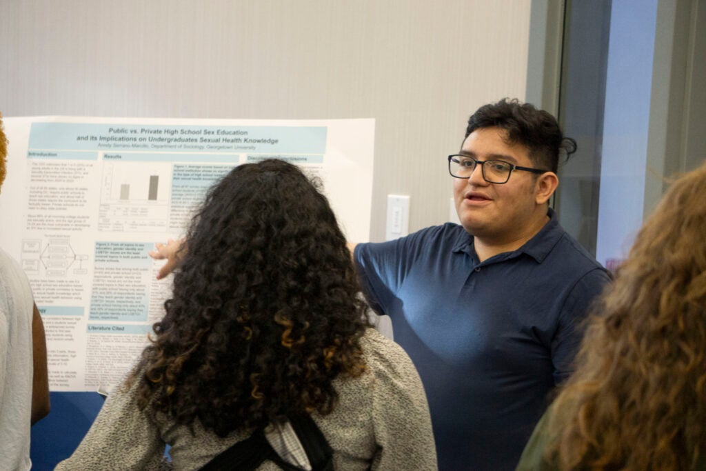 Senior Anndy Serrano-Marcillo points at their presentation while addressing a community member