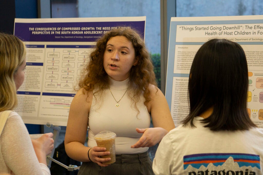 Senior Karis Danner-McDonald discusses their thesis presentation with two community members