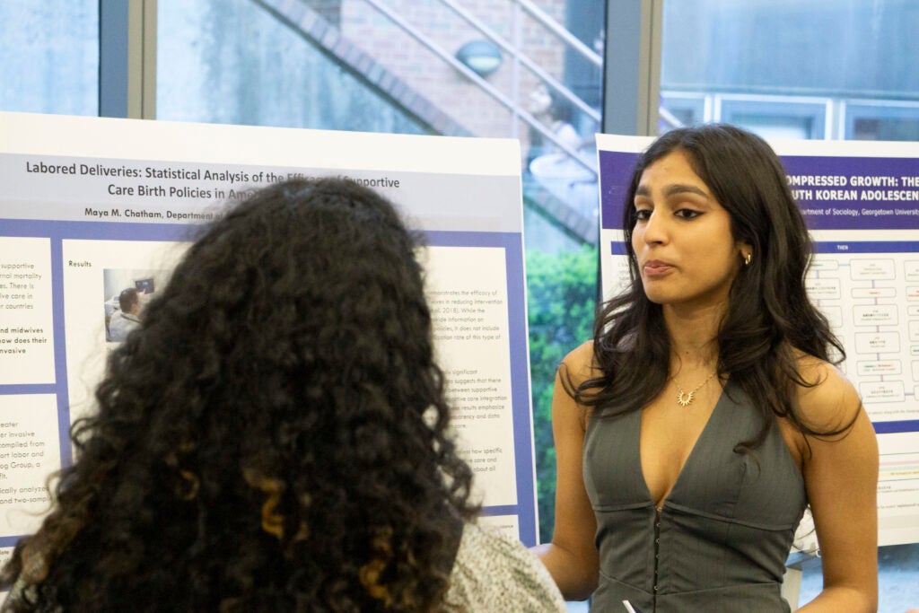 Senior Maya Chatham discusses their presentation with a community member